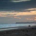 Couples walking along a beach at sunset in the Algarve region of Portugal.