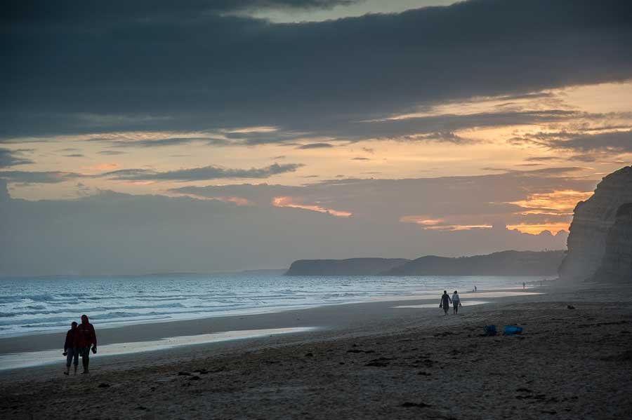 Couples walking along a beach at sunset in the Algarve region of Portugal.