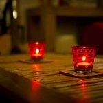 Two lit candles contained in a patterned red glass on a table.