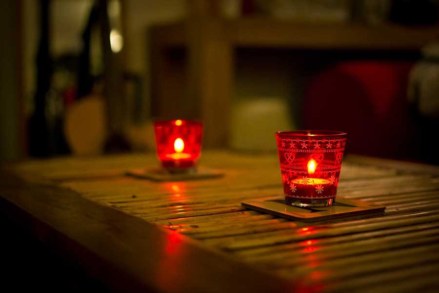 Two lit candles contained in a patterned red glass on a table.